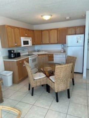Una cocina compacta con armarios de madera, microondas, estufa, refrigerador y una mesa de comedor con sillas.