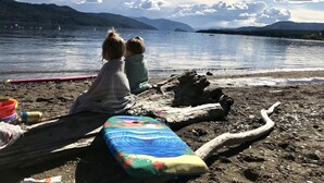 Dos personas sentadas en la playa, con una alfombra colorida y un tronco cerca.