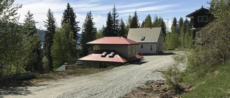Een huis met twee verdiepingen, met een rood dak, omgeven door bomen en een grindpad.