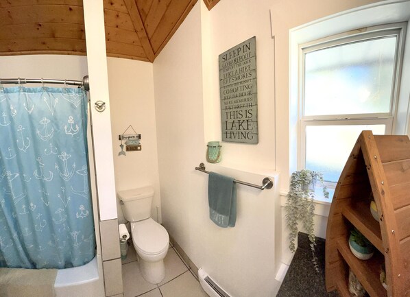 A bathroom with a shower curtain, toilet, towel rack, and a sign on the wall.