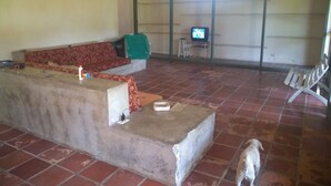 Una sala de estar con sofá, televisión sobre un mueble bajo, un perro y piso de baldosas.