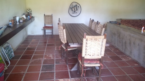 Un comedor con una larga mesa de madera y sillas de mimbre, un emblema en la pared y suelo de baldosas.