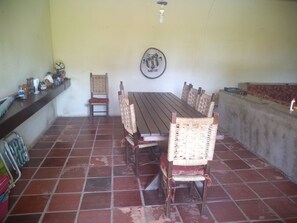 A dining area with a long wooden table and wicker chairs, a wall-mounted emblem, and a tiled floor. - House in Guarujá with 5 suites... one block from the beach. (Balneario Praia do Pernambuco)