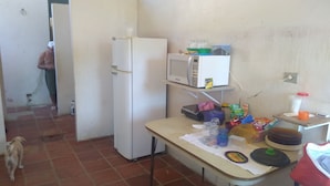 Una cocina con refrigerador, microondas y varios alimentos sobre la encimera.