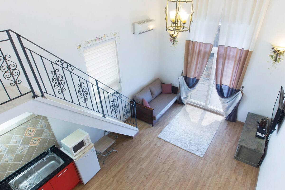 Un apartamento moderno con cocina, sala de estar con sofá y cortinas, una escalera y comedor.