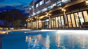 A hotel with a swimming pool, outdoor seating, and a well-lit facade. - Pool Villa Linderburg (Taean)