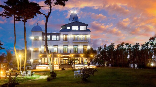 A large, multi-story hotel with a prominent tower and a well-lit entrance. - Pool Villa Linderburg (Taean)