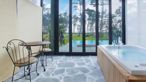 A modern bathroom with a stone floor, a wooden bathtub, and a glass door leading to a pool area. - Pool Villa Linderburg (Taean)