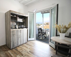 A modern kitchen with a wooden cabinet, a dining area with a table and chairs, and a sliding glass door leading to a balcony with a view. - Crystal View Mykonos (Mykonos)