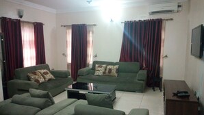 A living room with two sofas, a coffee table, and a TV on a stand. - Bayse One Place Jericho (Ibadan)