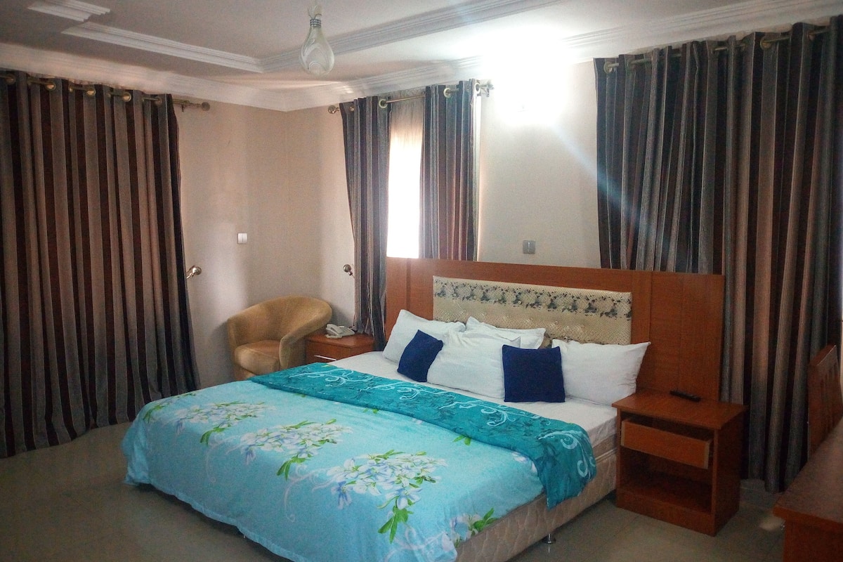 A hotel room with a bed, a chair, a nightstand, and curtains.