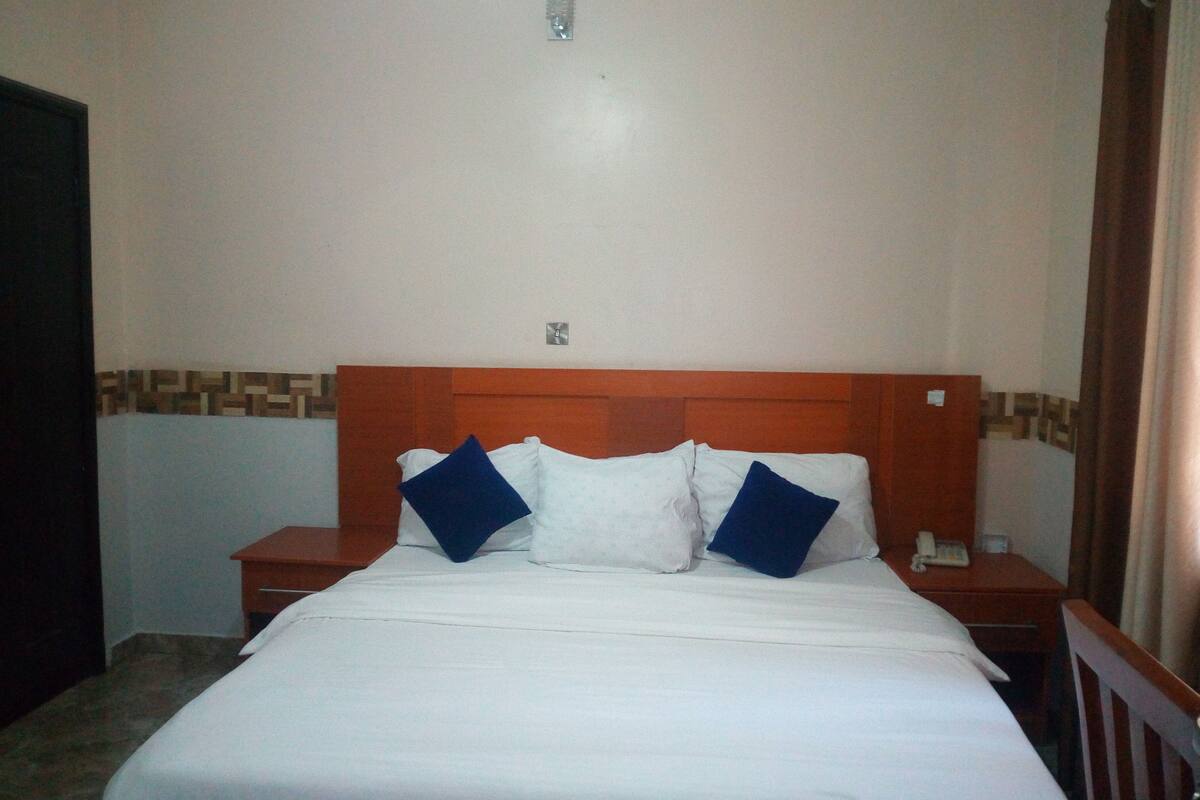A hotel room with a wooden headboard, white bedding, and two blue pillows.