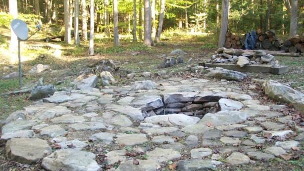 A stone fire pit surrounded by rocks in a forested area.