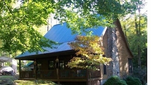 A cabin with a covered porch, a sloped roof, and a stone foundation.