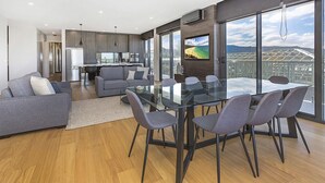 A modern living room with a glass dining table, grey sofas, and a kitchen in the background. - Cosmopolitan@SoHo -  amazing views (Gerringong)