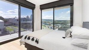 A bedroom with a large bed, a view of a cityscape through floor-to-ceiling windows, and a balcony with a glass railing. - Cosmopolitan@SoHo -  amazing views (Gerringong)