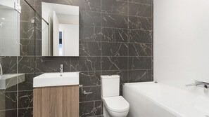 A modern bathroom with a marble backsplash, a white sink, a toilet, and a bathtub. - Cosmopolitan@SoHo -  amazing views (Gerringong)