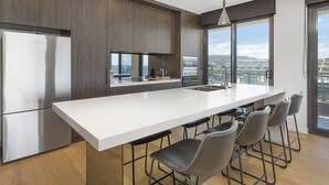 A modern kitchen with a large island, bar stools, stainless steel appliances, and a view through large windows. - Cosmopolitan@SoHo -  amazing views (Gerringong)