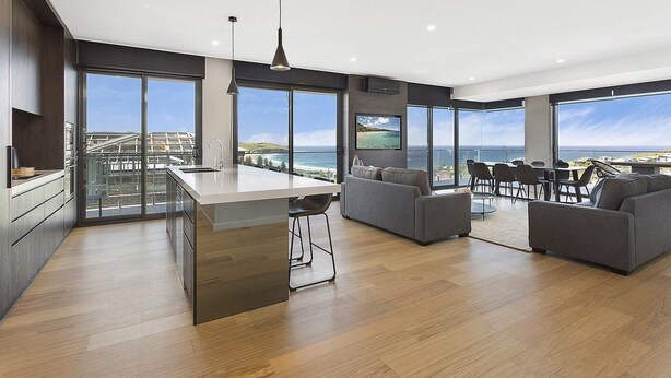 A modern kitchen with a large island, a dining area with a view, and a living room with a sofa and chairs. - Cosmopolitan@SoHo -  amazing views (Gerringong)