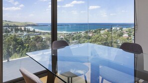 A modern room with a glass table and chairs, offering a view of a coastal town and ocean. - Cosmopolitan@SoHo -  amazing views (Gerringong)