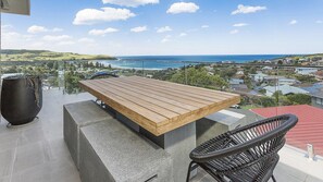 A balcony with a wooden table and chairs, overlooking a coastal town and ocean. - Cosmopolitan@SoHo -  amazing views (Gerringong)