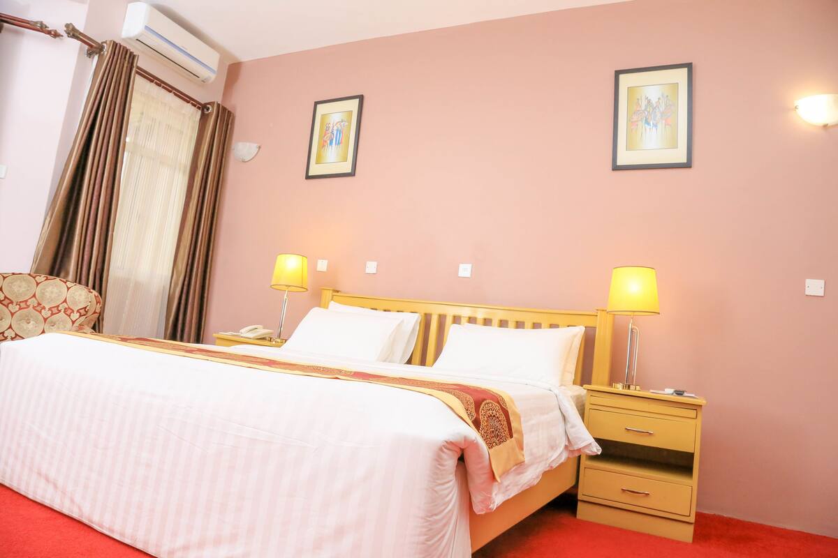 A hotel room with a bed, two bedside lamps, a nightstand, and a wall-mounted air conditioner.