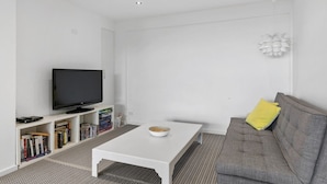 A modern living room with a flat-screen TV, a white coffee table, a grey sofa, and a bookshelf with books.