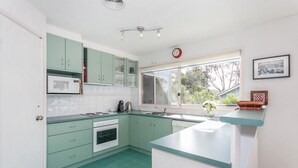 A kitchen with teal cabinets, a microwave, a sink, and a window with a view of greenery.