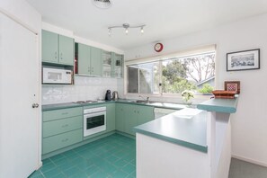 A kitchen with teal cabinets, a microwave, a sink, and a window with a view of greenery.