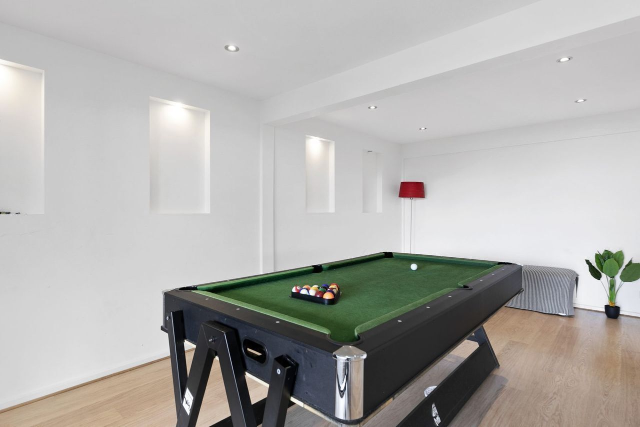 Una mesa de billar con bolas en el centro de una habitación con paredes blancas y suelo de madera.