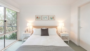 A hotel room with a large bed, two bedside tables, a window with a view, and three framed pictures on the wall.