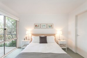 A hotel room with a large bed, two bedside tables, a window with a view, and three framed pictures on the wall.