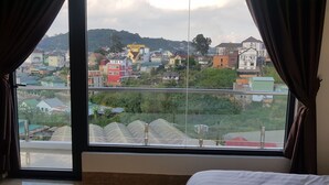 A room with a large window overlooking a cityscape with various buildings and greenery. - An Nhien Hotel (Xuan Huong - Da Lat)