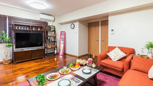Un salon doté d’un téléviseur à écran plat, d’un meuble de rangement en bois, d’un canapé orange et d’une table à manger mise avec des assiettes, des verres et une bouteille de vin.
