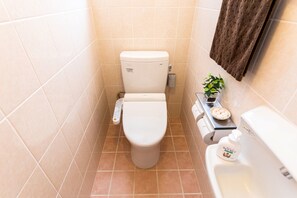 A small bathroom with a toilet, a sink, and a towel hanging on the wall. - Mizu House (Naha)