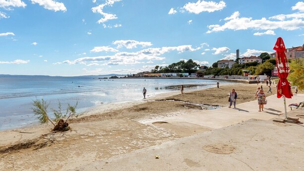 A beach with a clear sky, a few people walking, and a red umbrella on the right. - Rooms Jasenka, (15960), Split, hr (Split)