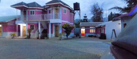 A pink building with a balcony, a water tank, and a paved courtyard.