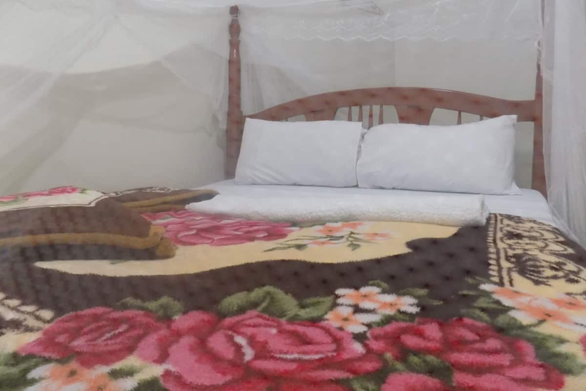 Cama com colcha florida, almofadas brancas e cabeceira de madeira.