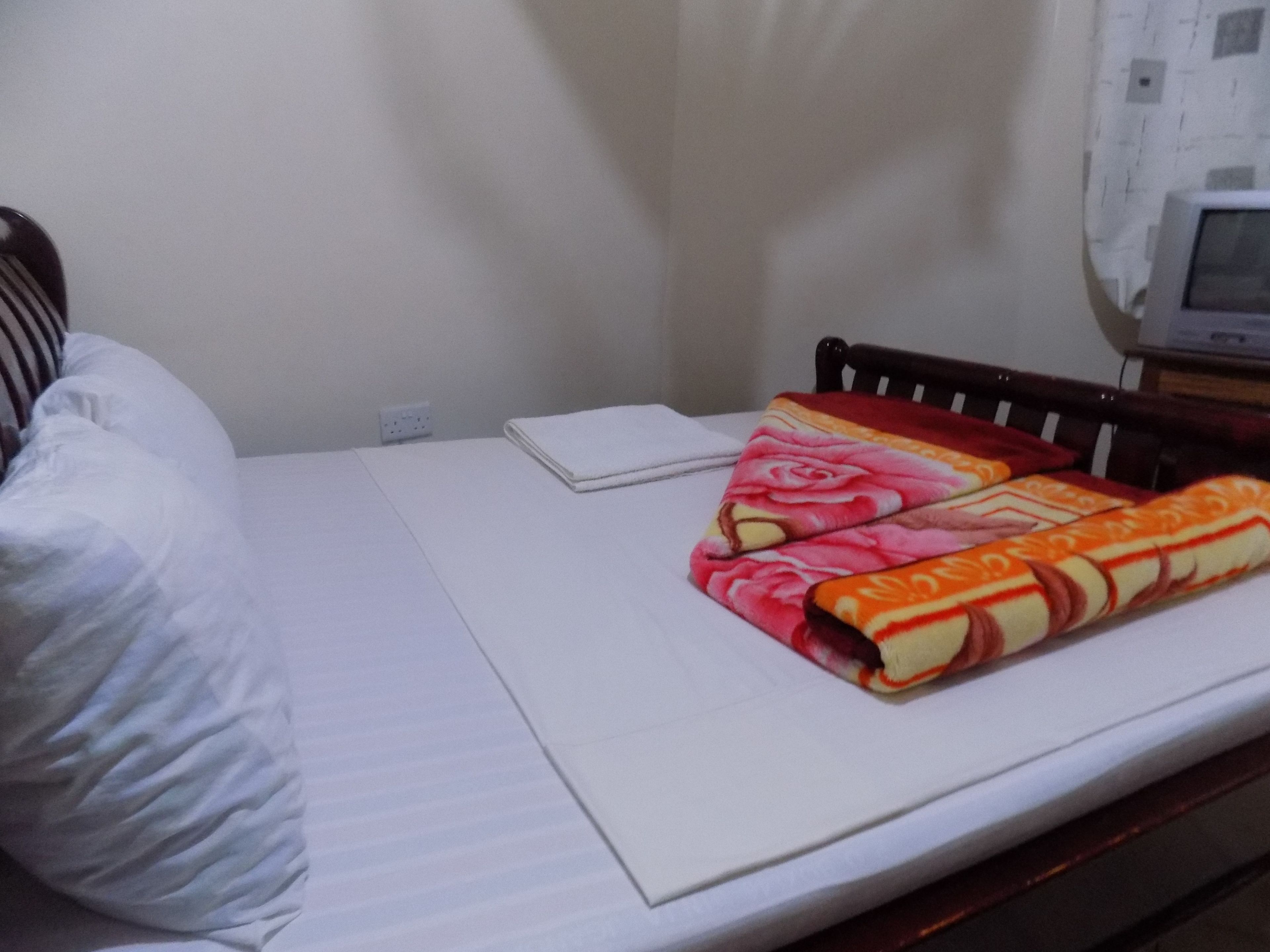 A bed with white linens, a folded blanket with a floral pattern, and a bedside table with a white object on it.