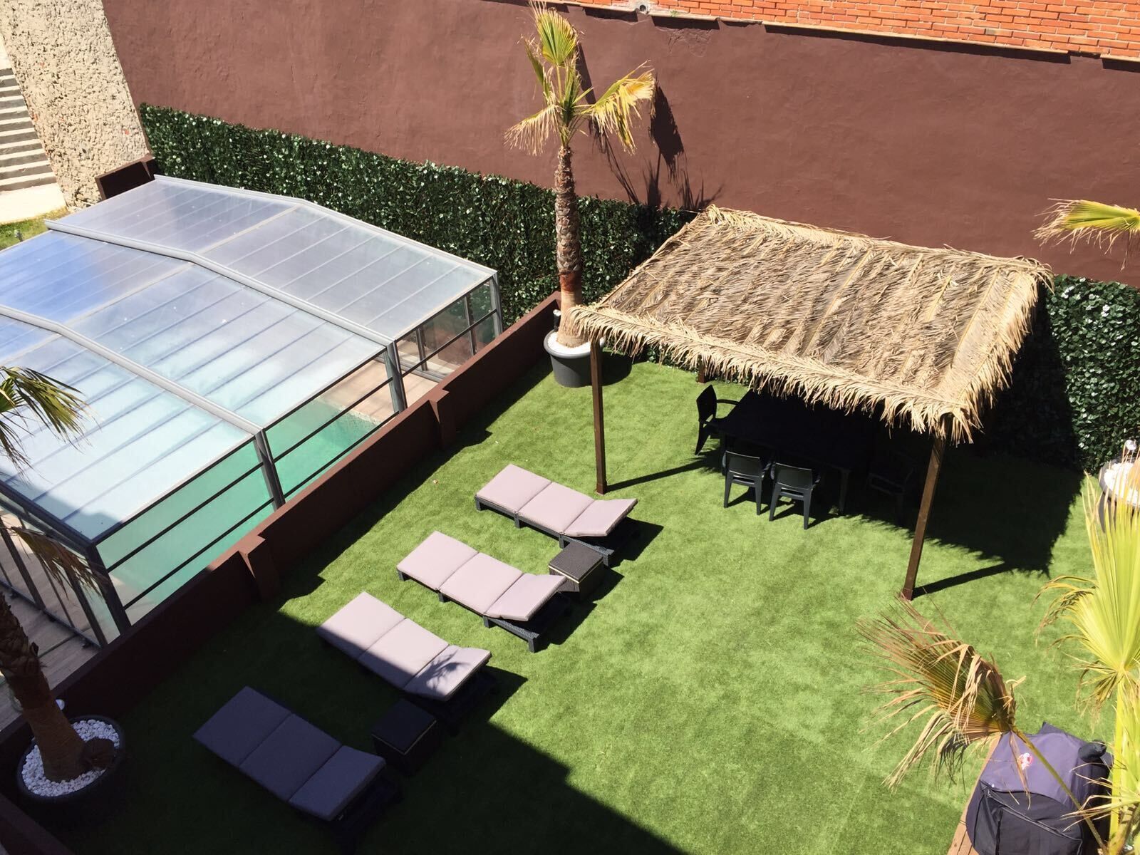 A rooftop pool with glass walls, a thatched umbrella, and outdoor seating.