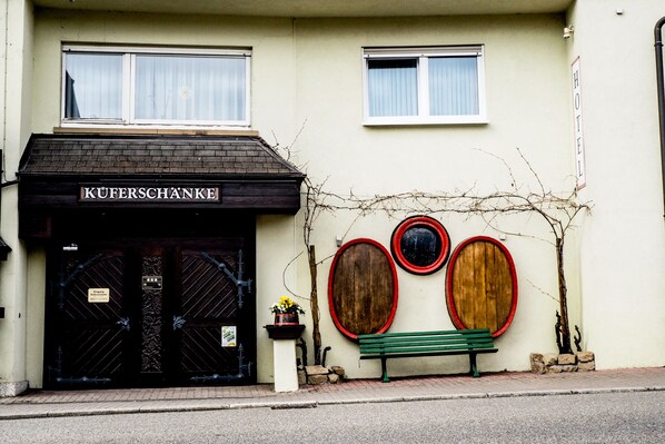 A hotel facade with a black entrance, a sign reading "KÜFERSCHANKE," and a bench with a circular wooden design on the wall. - Küferschänke (Sinsheim)