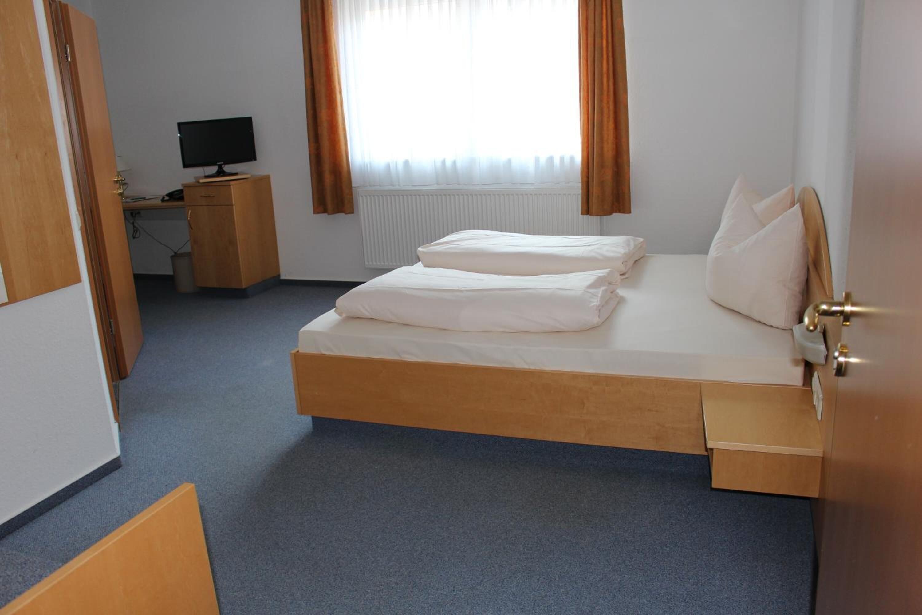 A hotel room with a single bed, a desk with a computer, and a window with curtains.