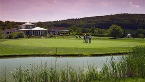 Un campo de golf con un estanque, una casa club y un paisaje montañoso al fondo.