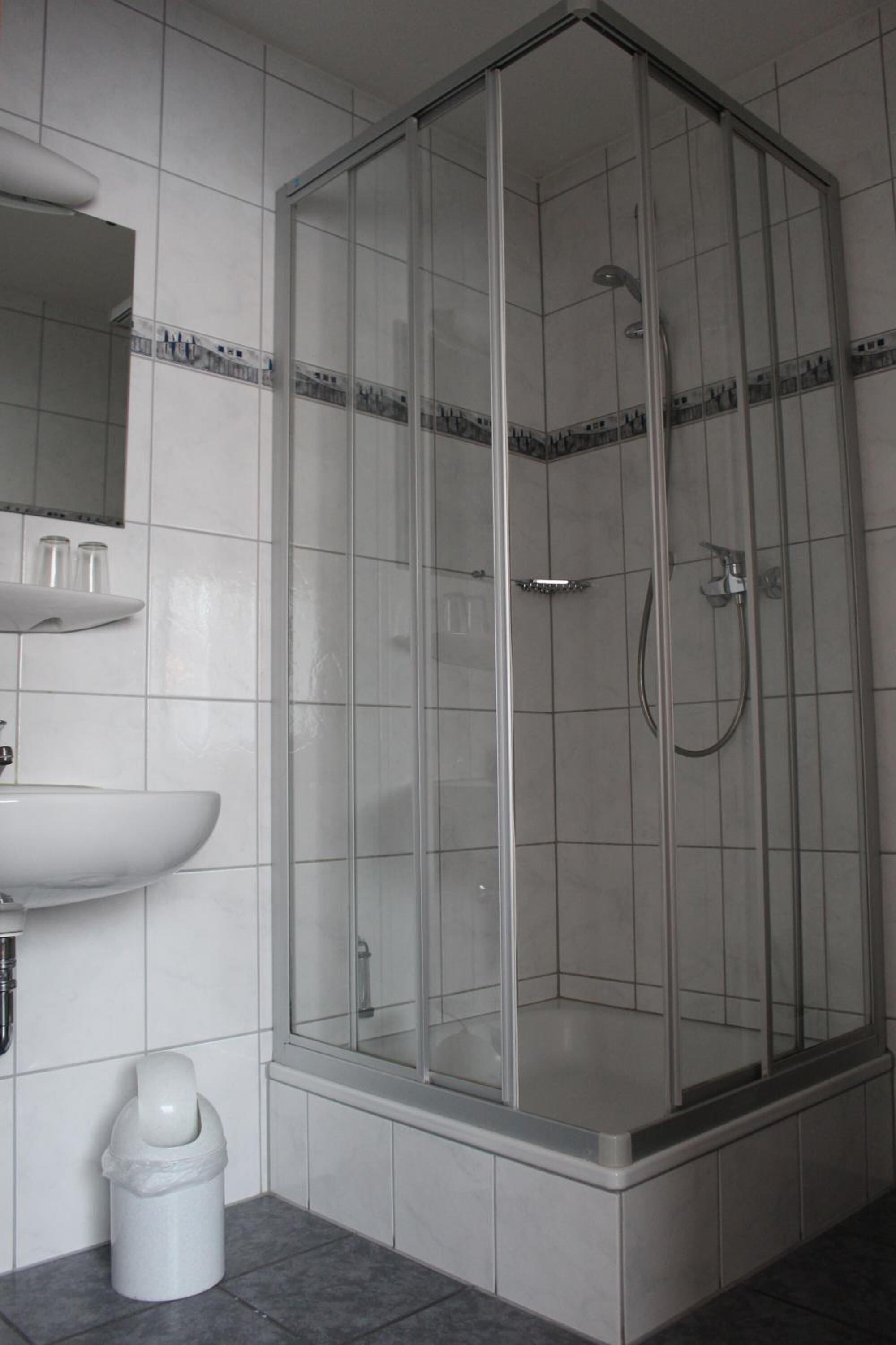 Ein modernes Badezimmer mit einer gläsernen Duschkabine, einem weißen Waschbecken und einem Mülleimer.