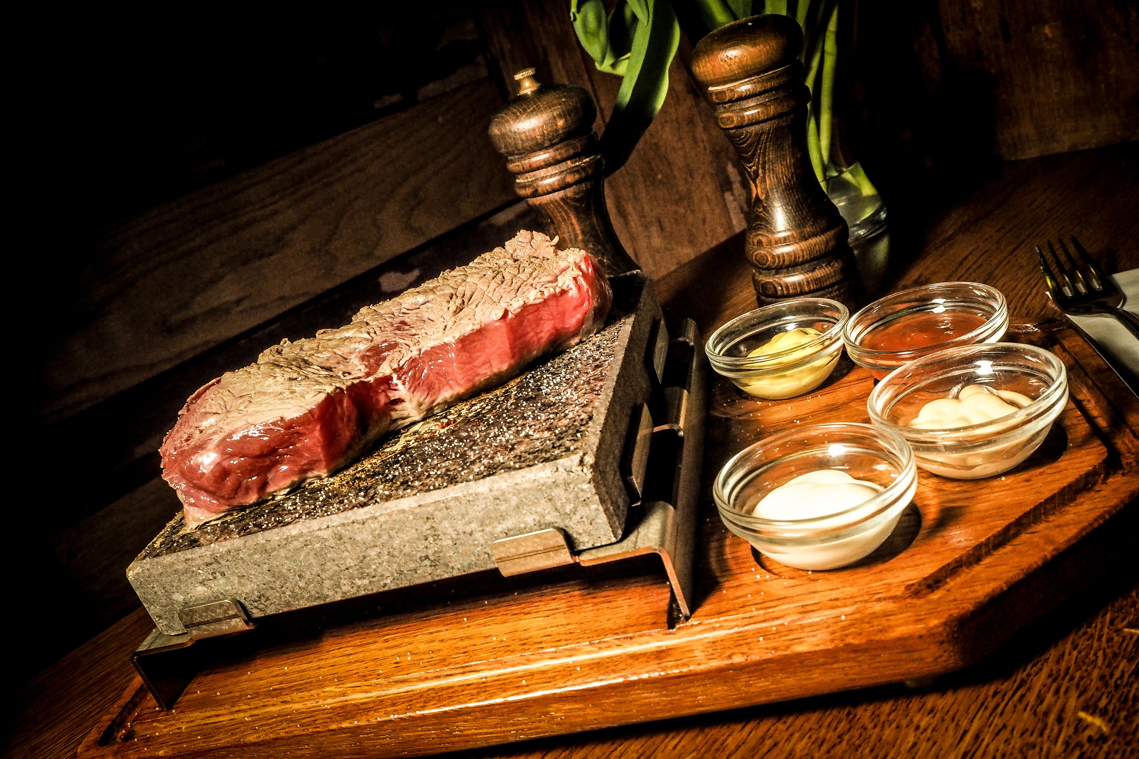 A steak on a cutting board with condiments and a knife.