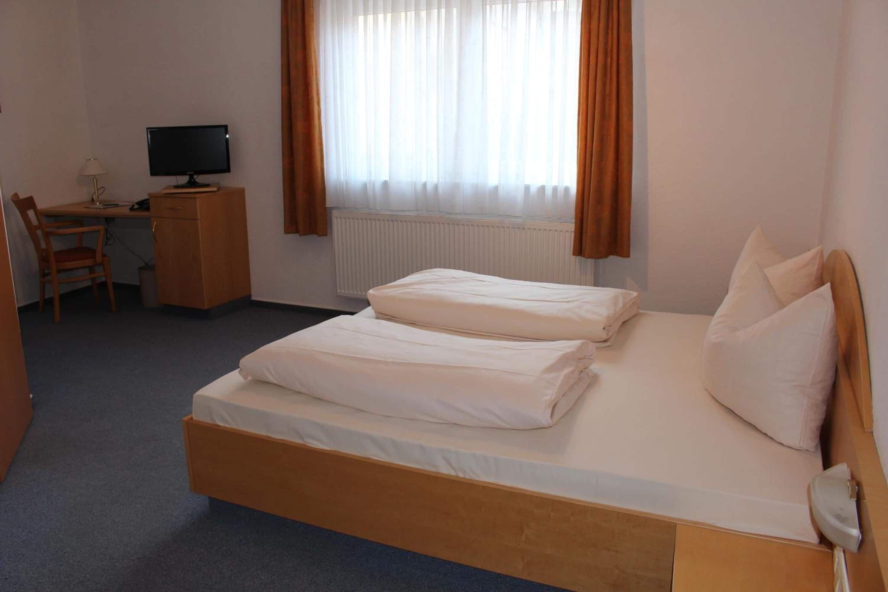 Ein Hotelzimmer mit einem Einzelbett, einem Schreibtisch mit Computer und einem Stuhl.