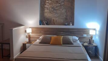 A bedroom with a large bed, two bedside tables with lamps, a stone wall, and a wooden headboard.
