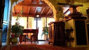 Un interior rústico con un arco de piedra, vigas de madera en el techo, una zona de comedor con mesa y sillas, y plantas en macetas.