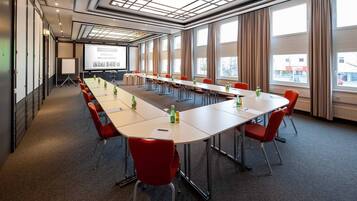 A conference room with a long table, red chairs, and a projector screen displaying a welcome message.