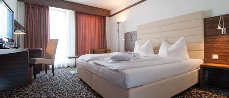 Habitación de hotel con una cama grande, un escritorio, una silla y un televisor.
